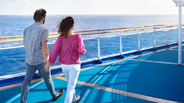 couple holding hands while they walk together on deck.