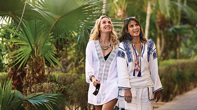 two women happily walking along a lush pathway