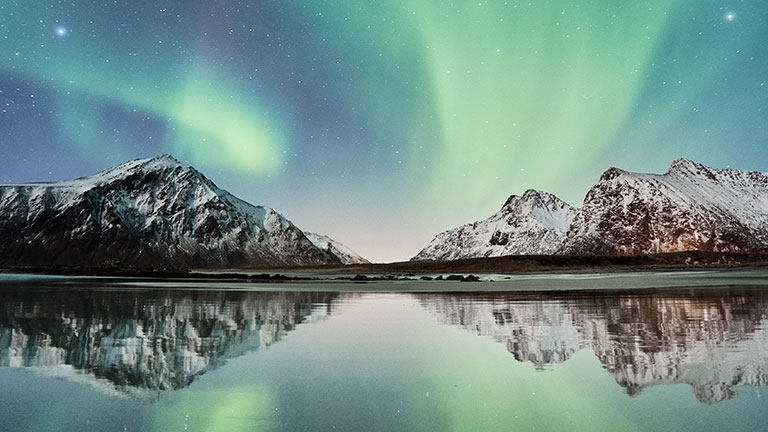 A greenish sky with snowy mountains behind the lake