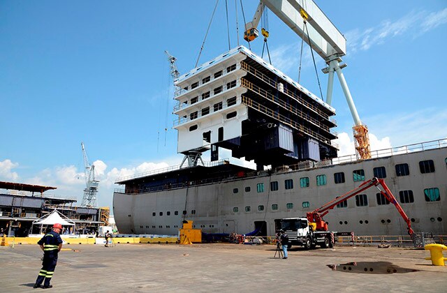 A crane lowering a section of staterooms onto a ship's keel.