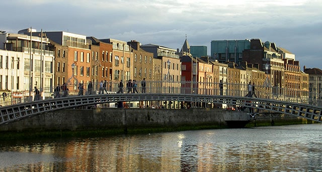 people walking over a bridge that goes across a river in a European town 